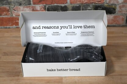 Open box showing the text "and reasons you'll love them" with four descriptions: "Advanced Protection", "Food Safe", "Easy to Clean", and "Temperature Resistant". Box has a pair of oven gloves inside. Box also says "bake better bread".
